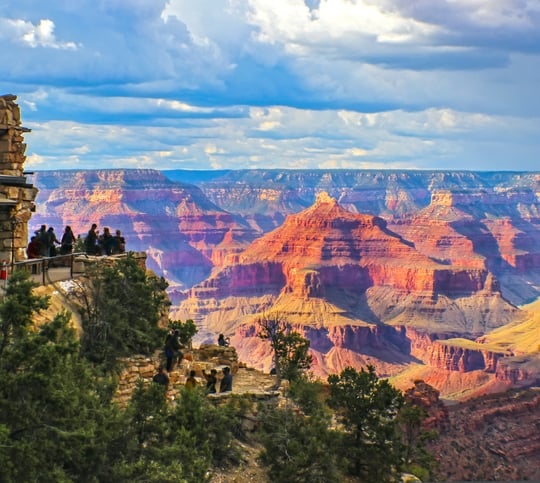 Grand Canyon South Rim view at golden hour under stormy sky with tourists at lookout point taking pictures and selfies